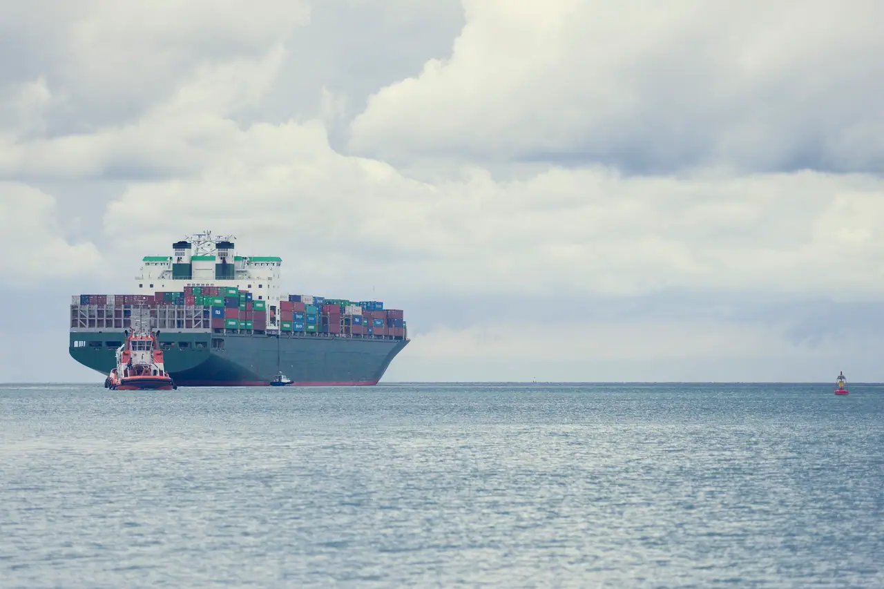 Porte-conteneurs à l'approche d'un port, accompagné d'un remorqueur